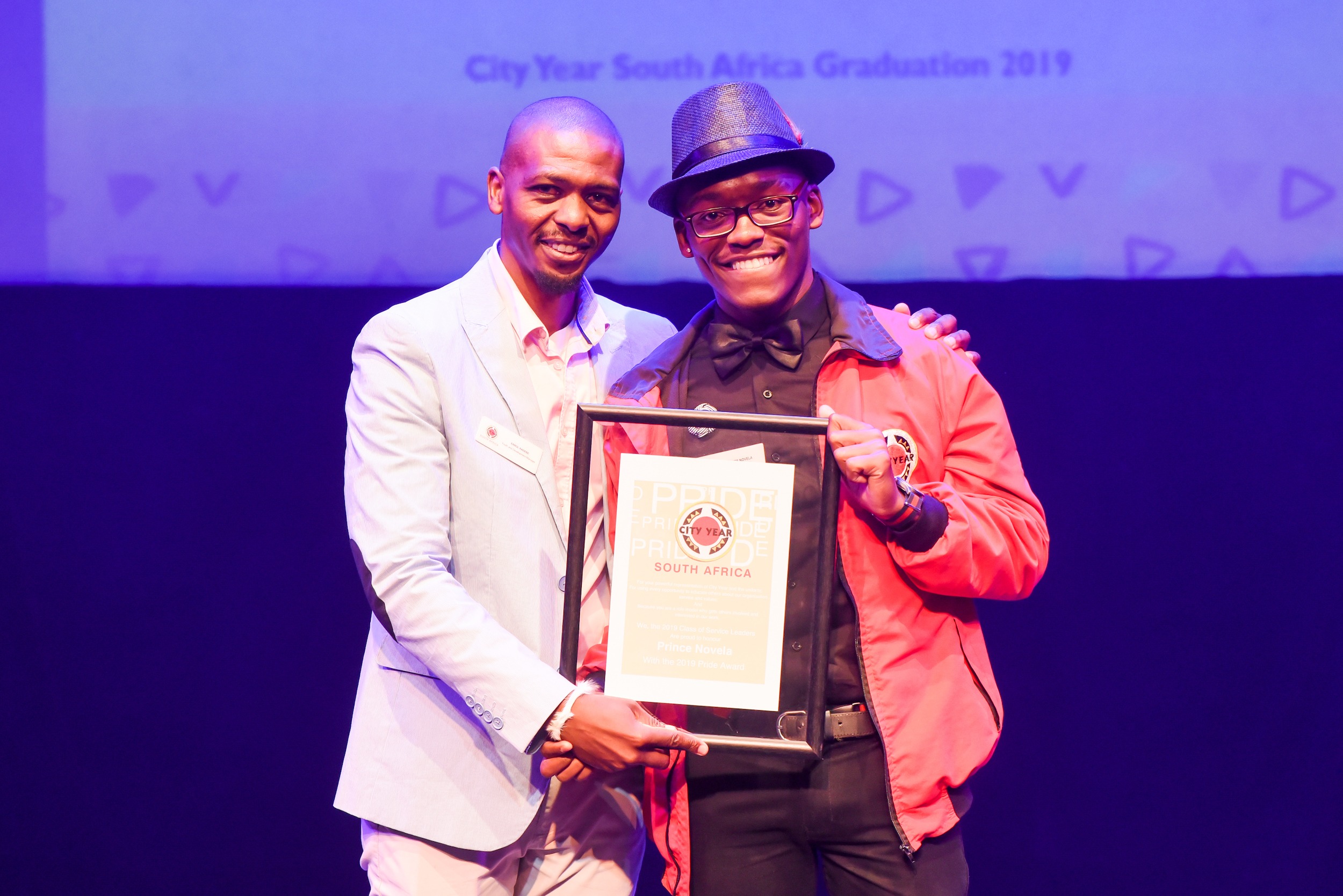 Staff member with his arm around a service leader holding an award onstage