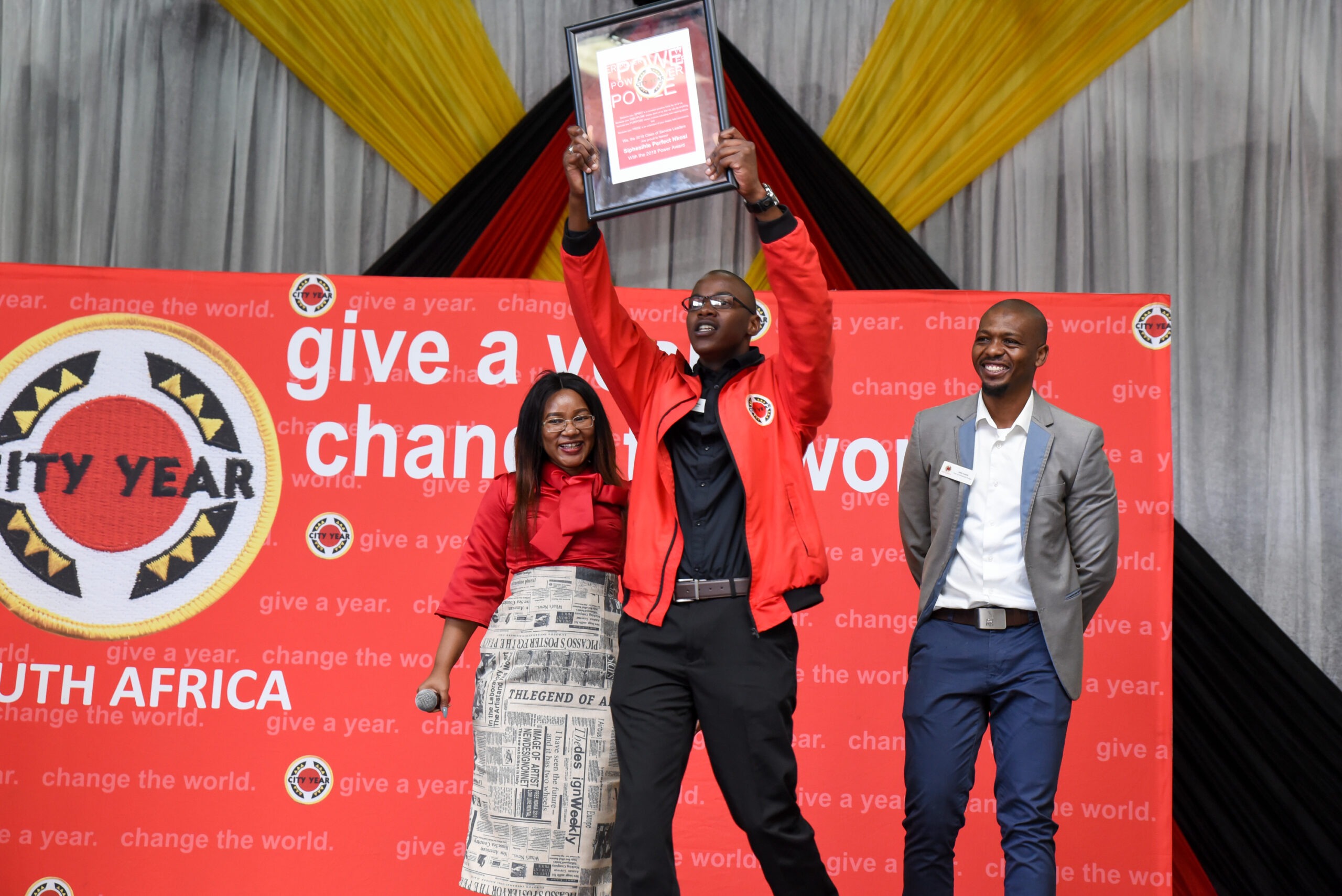 Two City Year staff members next to a service leader holding an award onstage